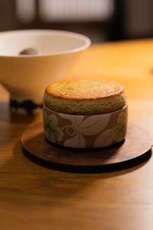 A decorative ceramic dessert bowl with floral pattern sits on a wooden coaster in warm lighting.