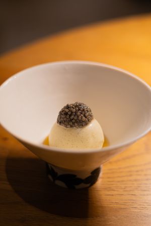 Modern plated dessert with white mousse and dark garnish in artistic bowl.