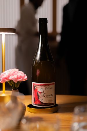 Wine bottles with pink and red labels displayed on wooden table under ambient lighting.