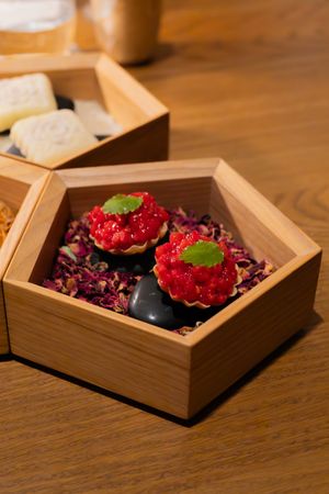 Fresh red berries presented in wooden hexagonal box with purple garnish.