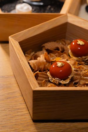 Decorative wooden box filled with dried leaves and red cherry tomatoes on a wooden table.
