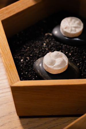 Meringue or white cookies arranged in a wooden serving tray with black stones or pebbles.