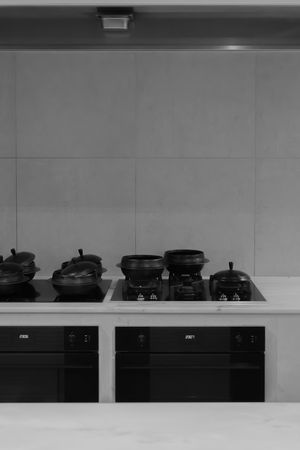 Black and white view of professional kitchen stovetop with multiple cooking vessels.