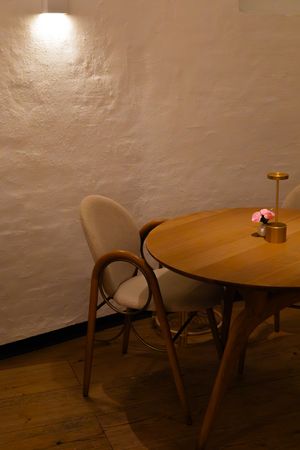 Simple wooden cafe tables and chairs arranged against a white textured wall in a minimalist restaurant setting.
