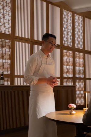 Chef in white uniform working in elegant restaurant interior with geometric patterned screens.
