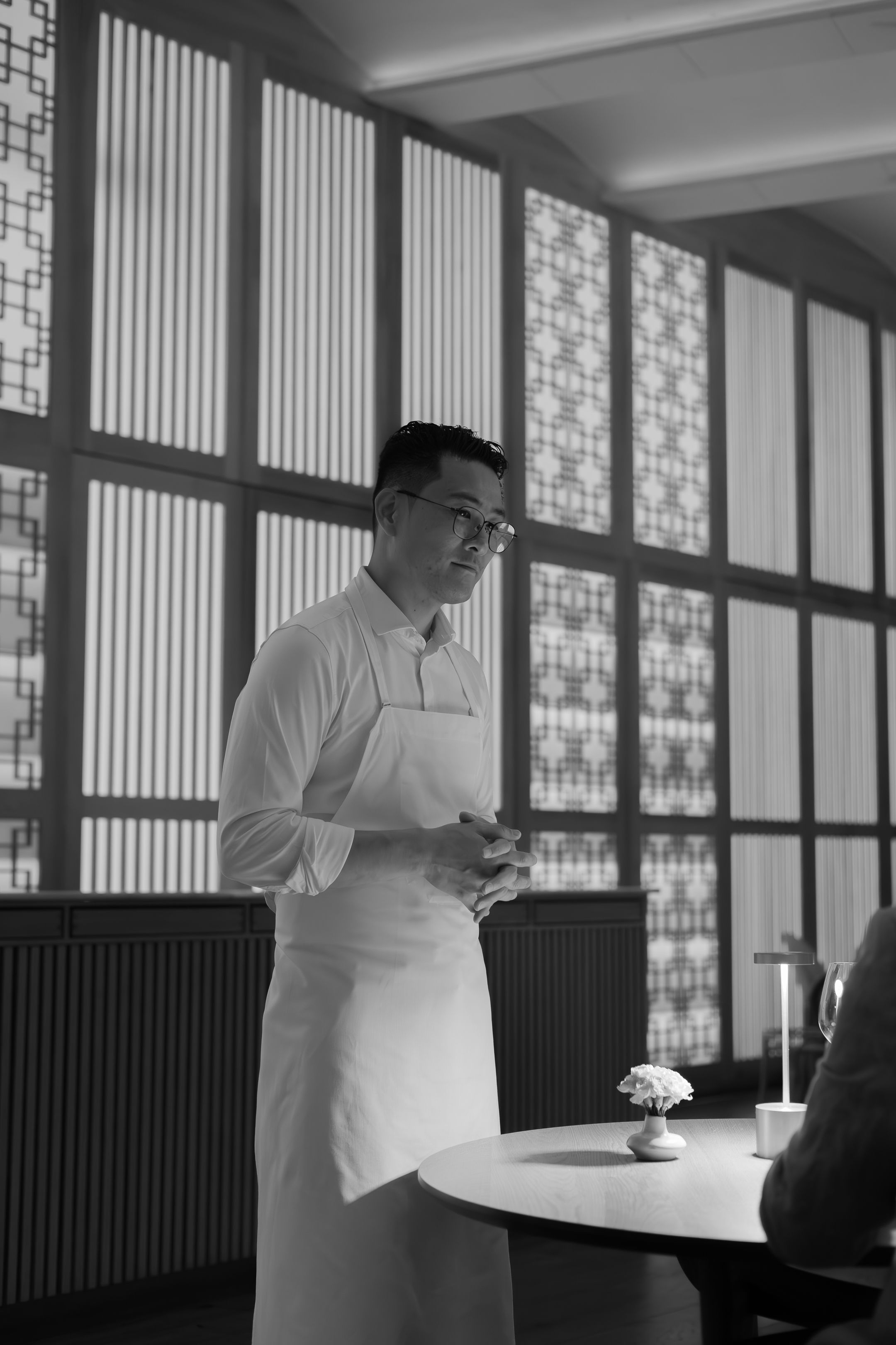 Restaurant interior with modern geometric window panels creating dramatic lighting patterns.