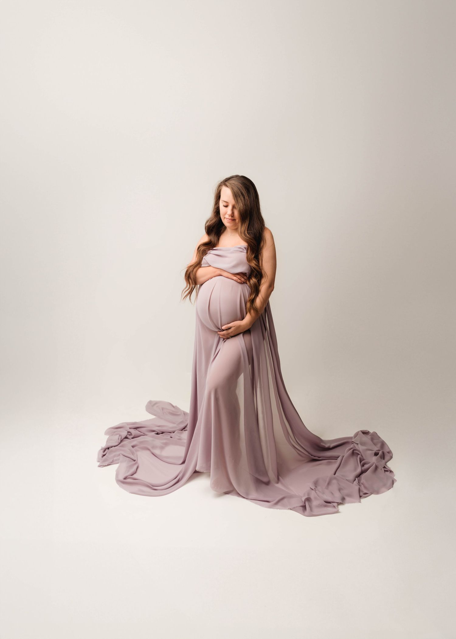 Artistic maternity photos featuring flowing mauve dress against neutral studio backdrop.