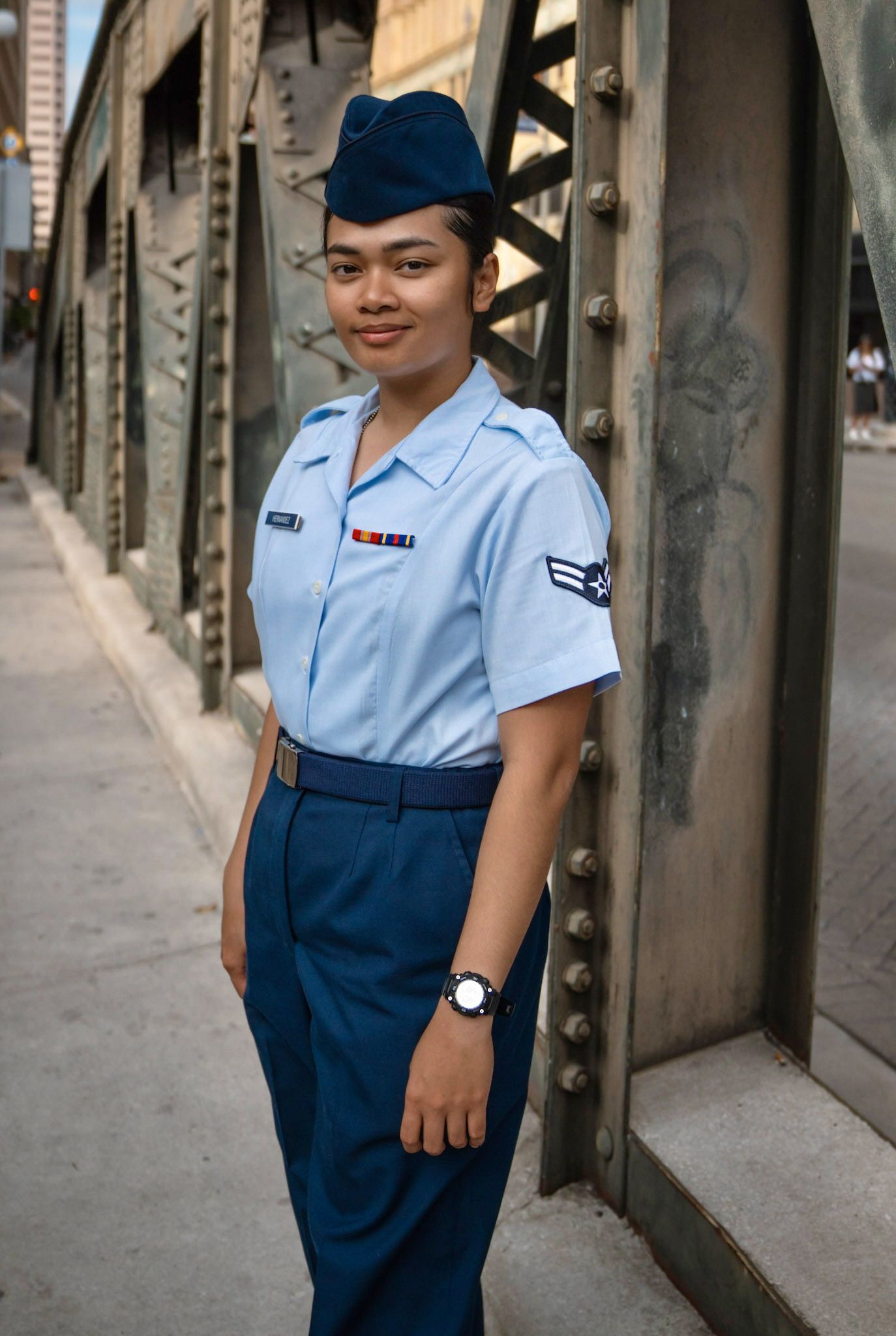 United States Air Force Airman in light blue shirt and dark trousers posing on a historic downtown bridge in San Antonio after graduation.