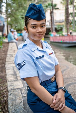 United States Air Force Airman in blue service uniform seated along the San Antonio River Walk after graduation.
