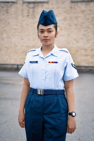 Air Force Airman in blue service uniform standing at attention outside a training facility at Lackland AFB.