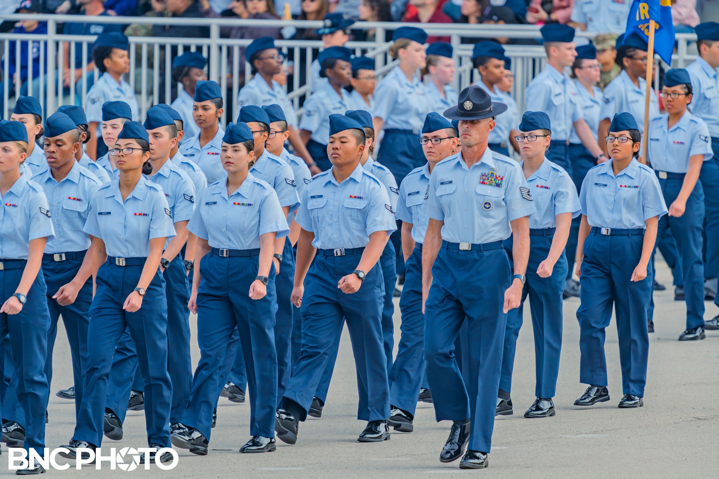 Air Force trainees marching in formation with a training instructor at the front during a basic military training ceremony.