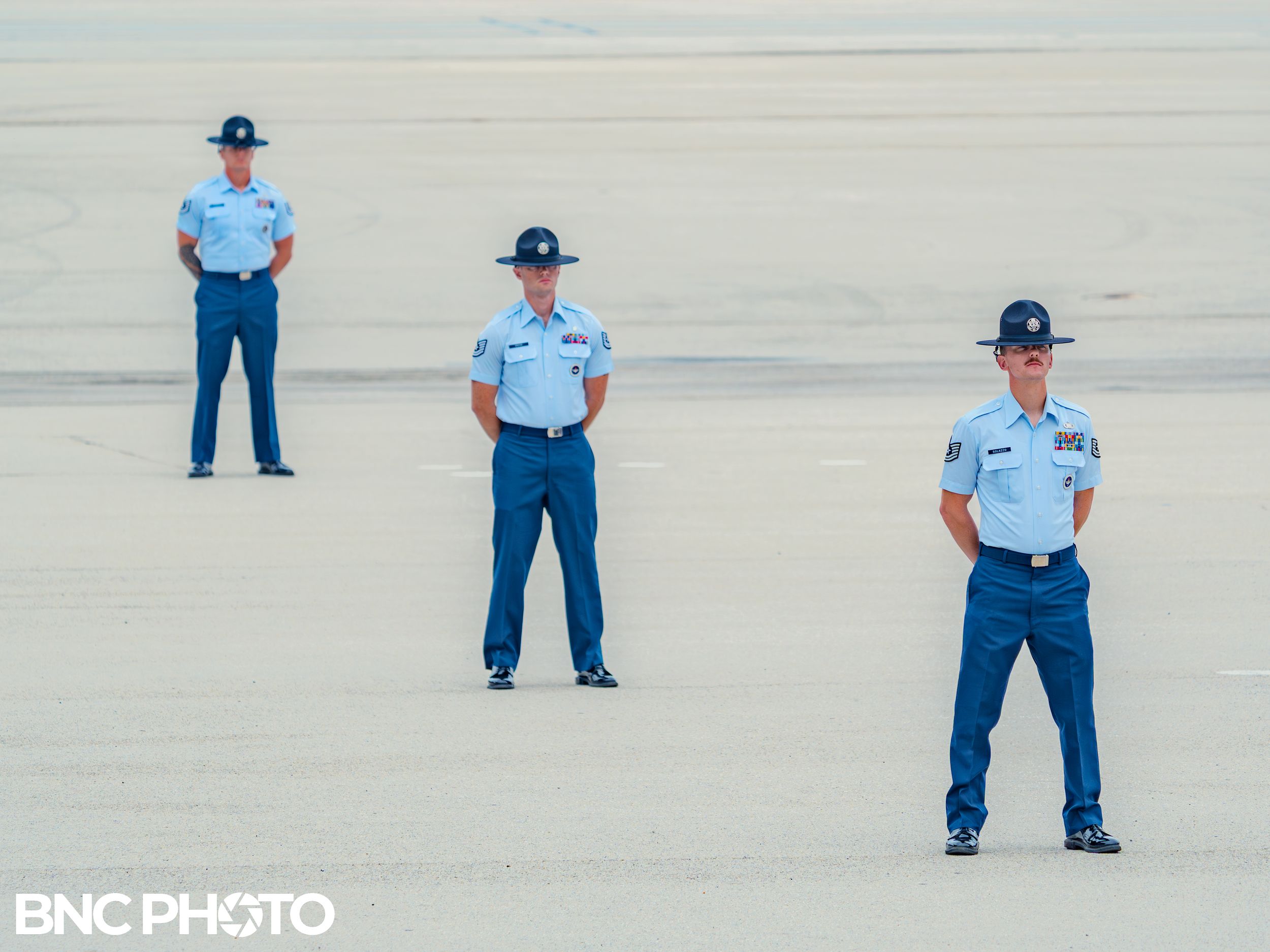 Three U.S. Air Force training instructors standing spaced apart on the parade field before a graduation ceremony