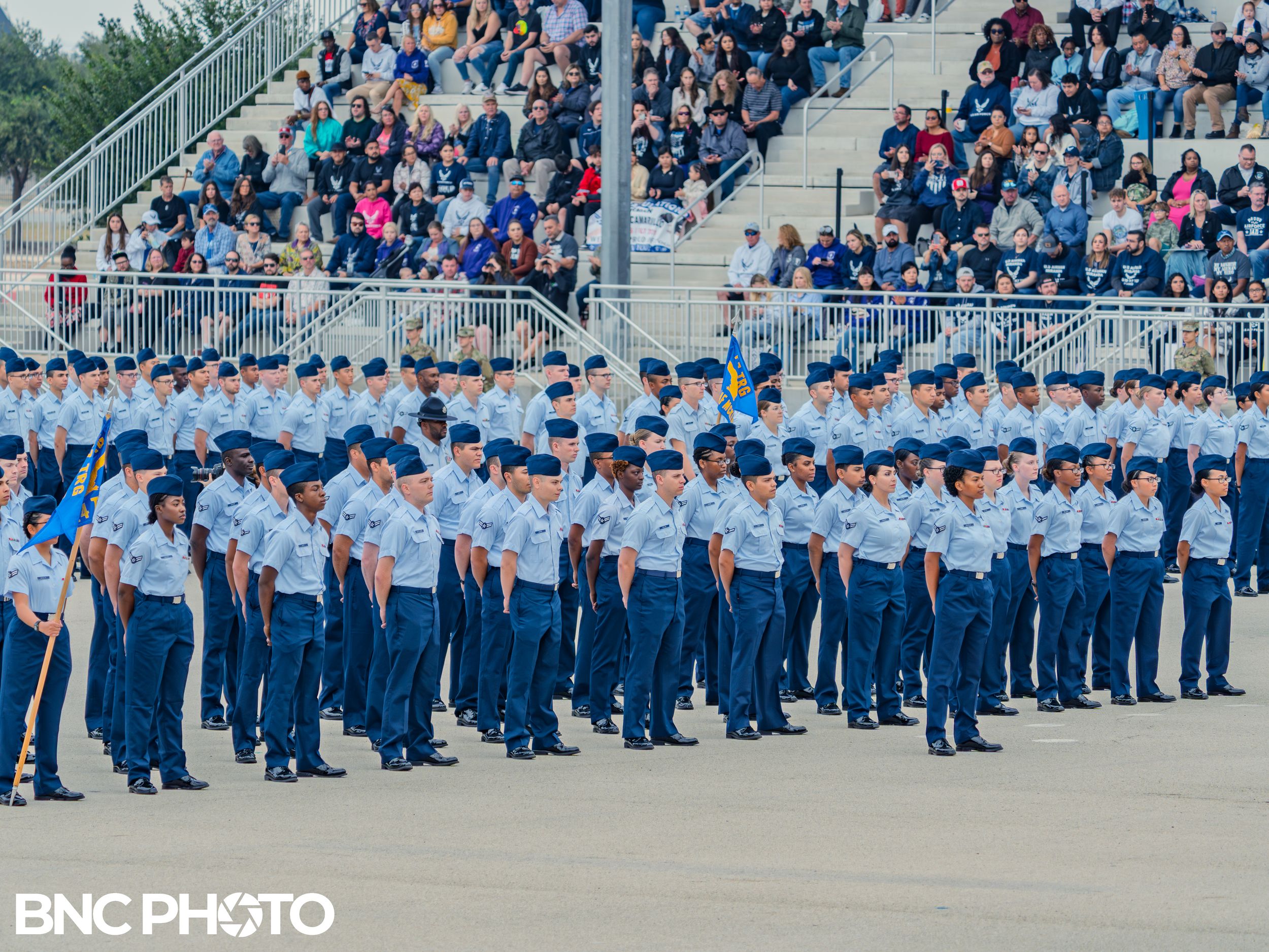 U.S. Air Force trainees assembled in formation in front of a seated audience during a basic military training graduation.