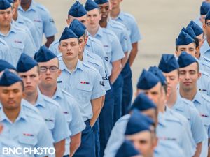 Row of Air Force trainees in light blue shirts and dark blue trousers standing in formation at a basic training graduation.