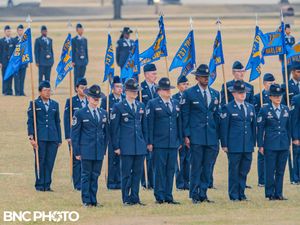 Group of U.S. Air Force instructors in dark blue service uniforms with flight flags lined up on the parade field at Lackland AFB.