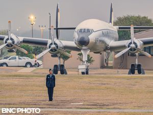 Single U.S. Air Force officer in dark blue service uniform standing at attention in front of a vintage aircraft on the parade field.