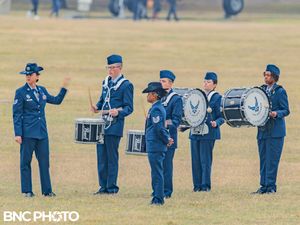 Air Force band members in dark blue service uniforms playing drums during a basic military training graduation.
