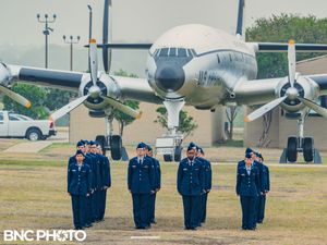 Smaller group of U.S. Air Force personnel in blue dress uniforms marching toward the camera during a graduation ceremony with a vintage plan