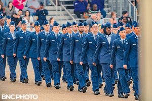 Smaller group of U.S. Air Force personnel in blue dress uniforms marching toward the camera during a graduation ceremony with a vintage plan