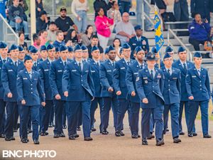 Group of U.S. Air Force graduates in blue dress uniforms standing in formation on the parade field at a military graduation.