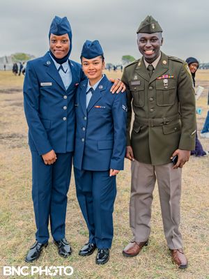 Three service members, two in U.S. Air Force dress uniforms and one in an Army service uniform, smiling and posing together after the gradua