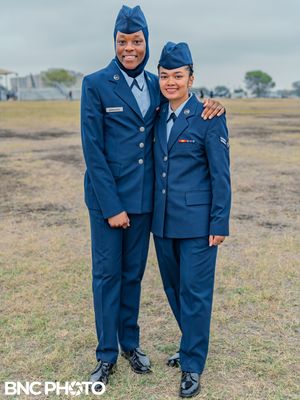 Two U.S. Air Force graduates in blue dress uniforms posing together and smiling on the parade field after the graduation ceremony.