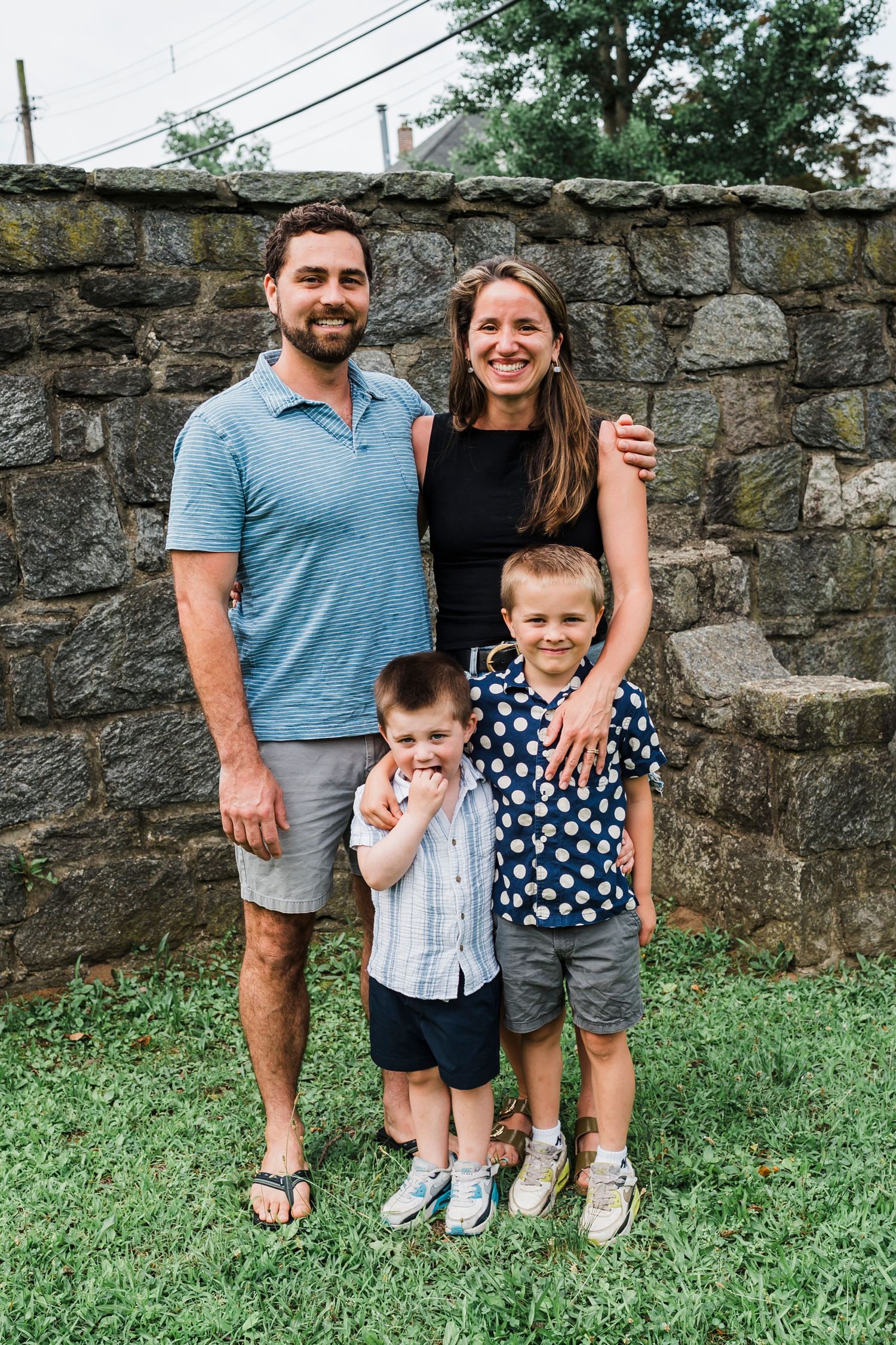 Family poses for photos together outdoors against stone wall, showing progression of poses from left to right.
