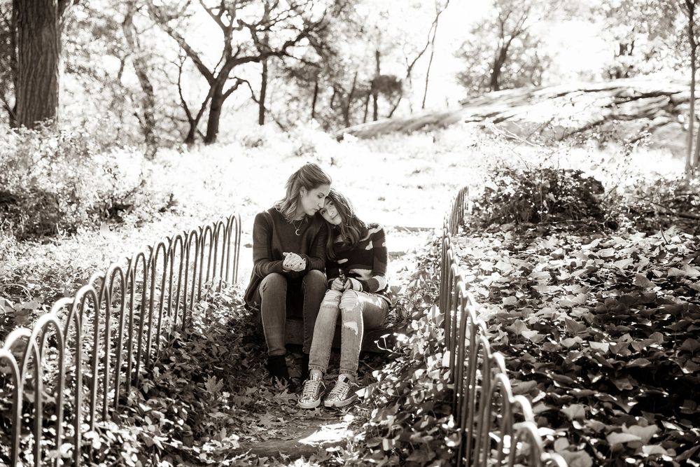 Black and white artistic portrait in a natural wooded setting with metal fencing.