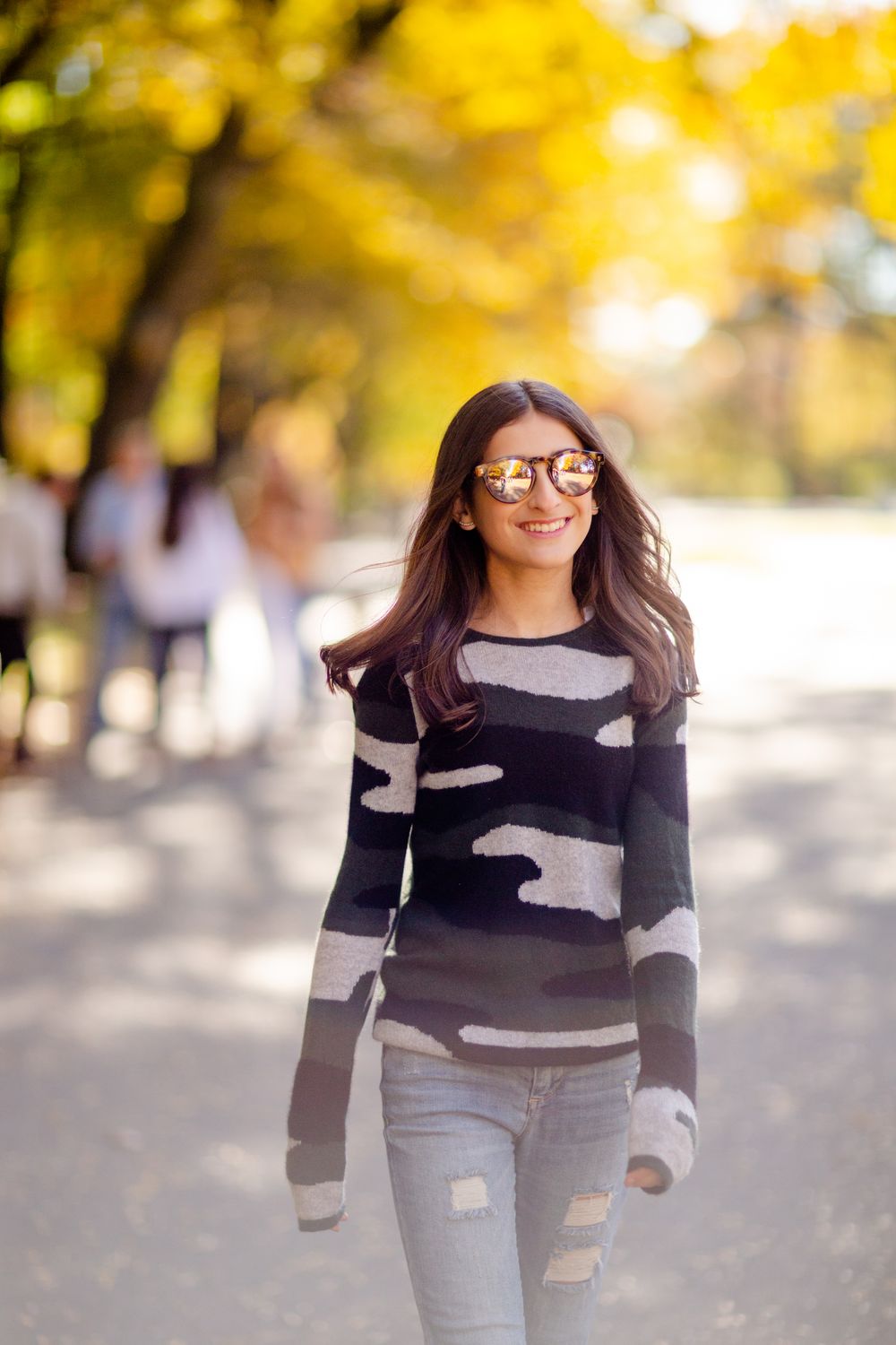 Person wearing glasses and striped sweater walks through fall foliage on sunny day.