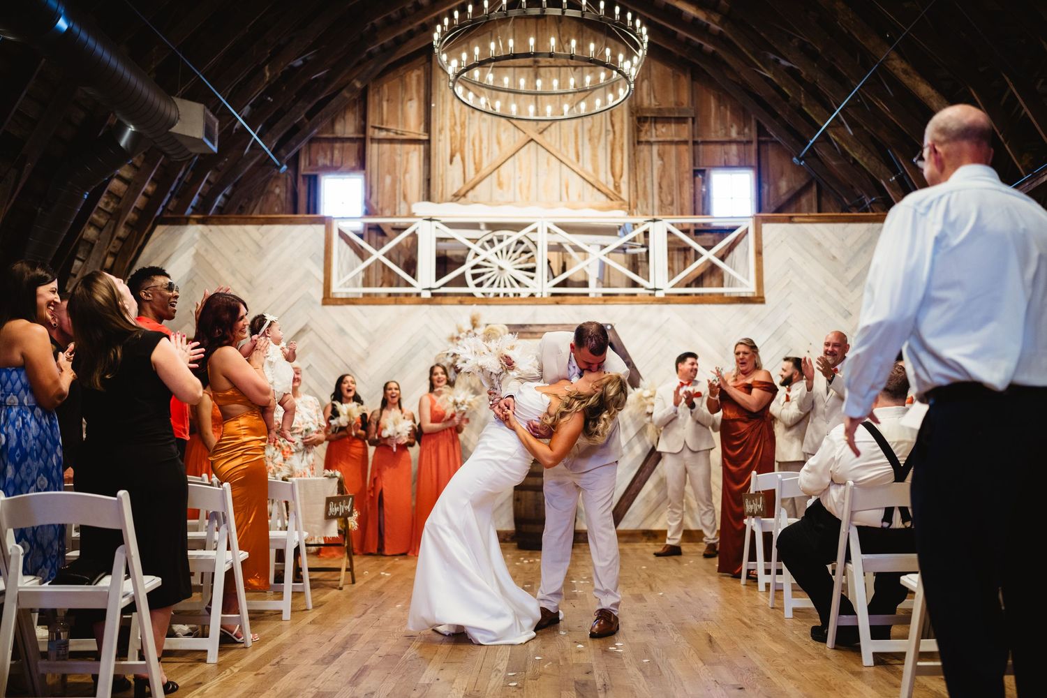 Wedding guests dancing under rustic string lights and wooden beams in a charming barn reception venue.