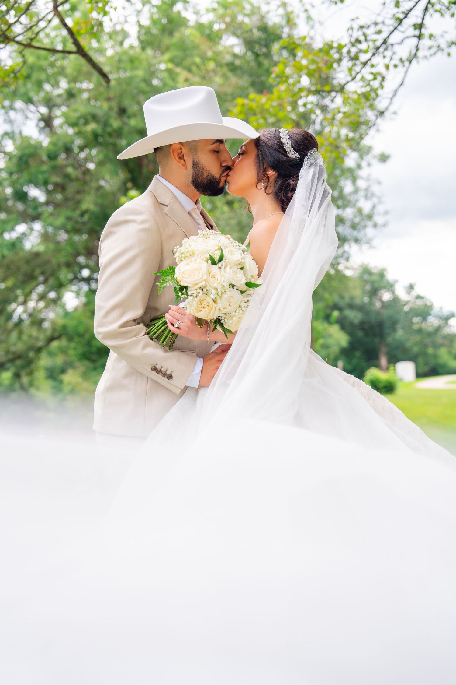 Newlyweds share intimate moment with white bouquet in garden setting.