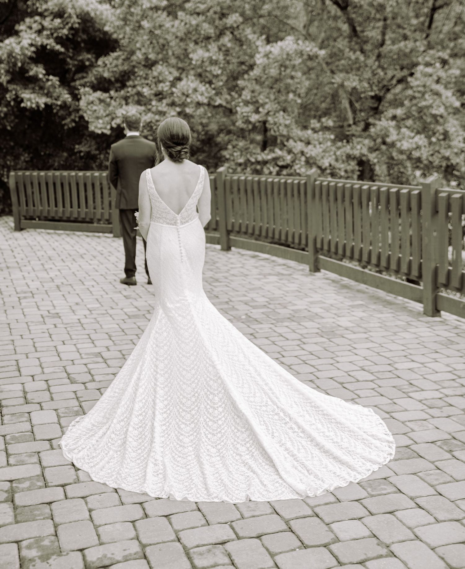 Elegant mermaid-style wedding gown with intricate lace detailing and dramatic train photographed on a brick pathway.