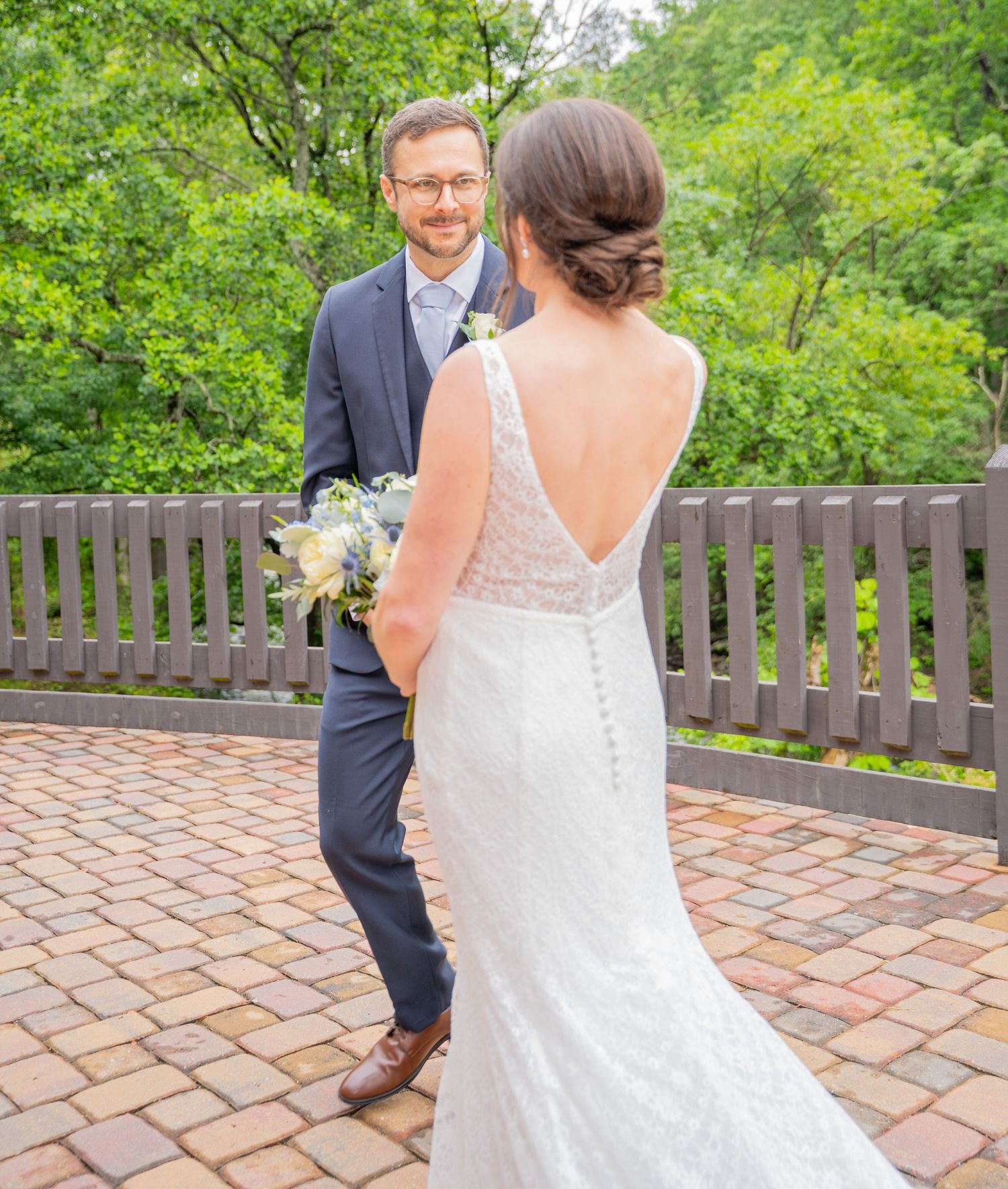 A romantic first look moment between newlyweds on a brick patio with lush greenery in the background.