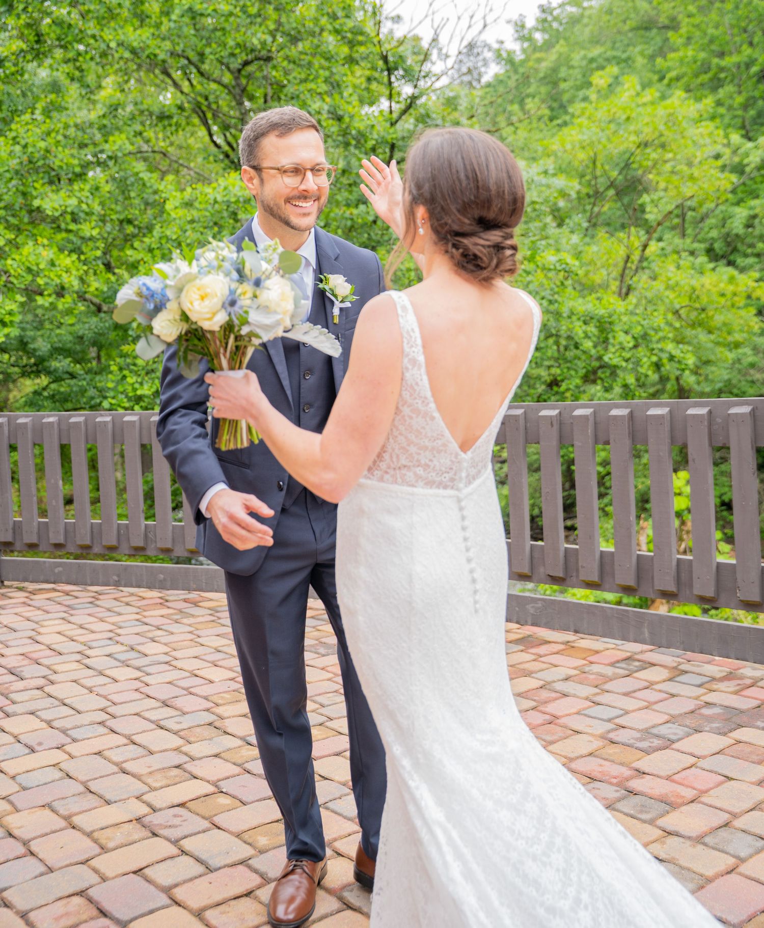 A couple in wedding attire share a joyful moment on a brick patio surrounded by lush greenery.
