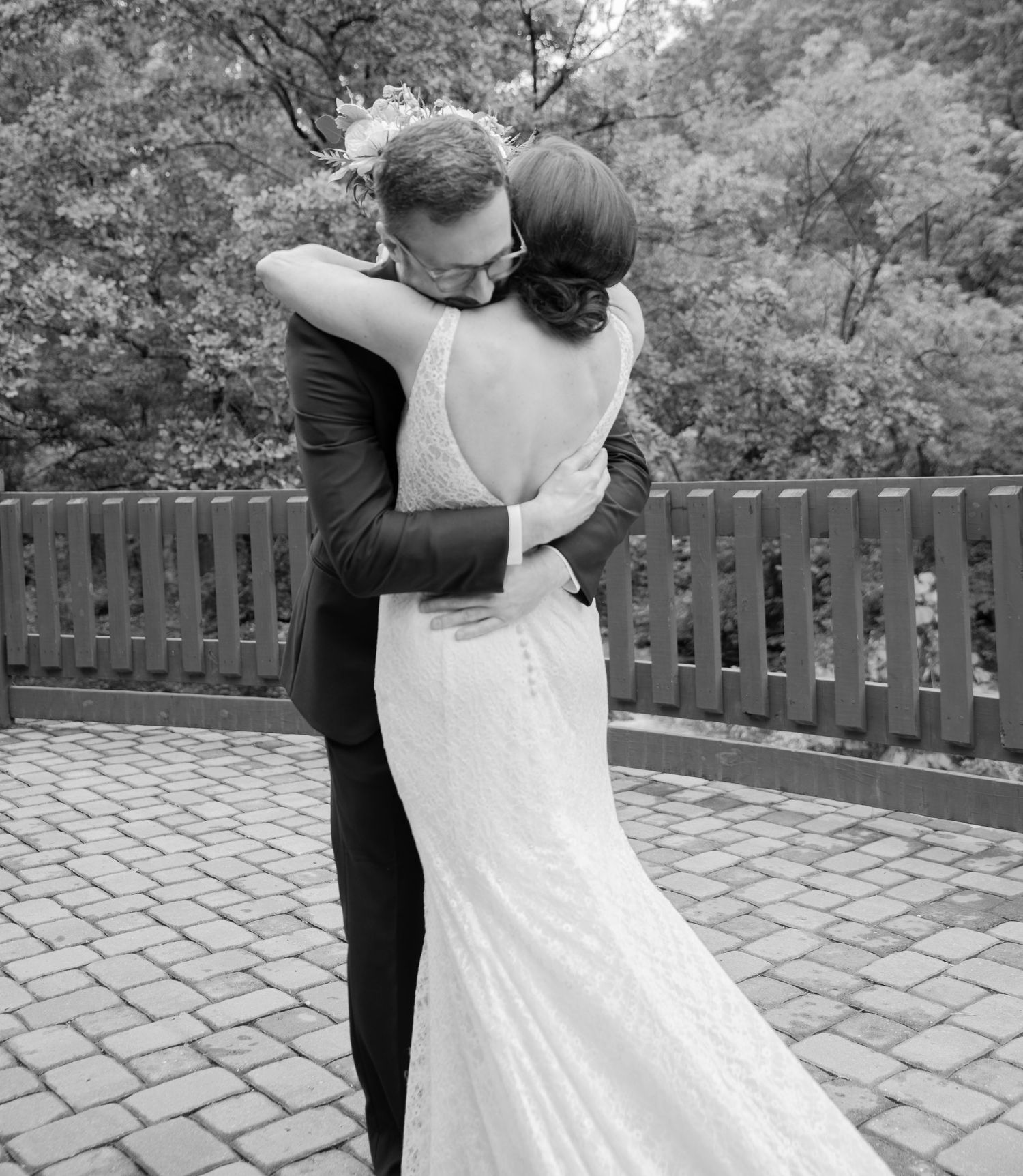 A tender embrace between a bride and groom during their wedding on a brick patio surrounded by wooden fencing.