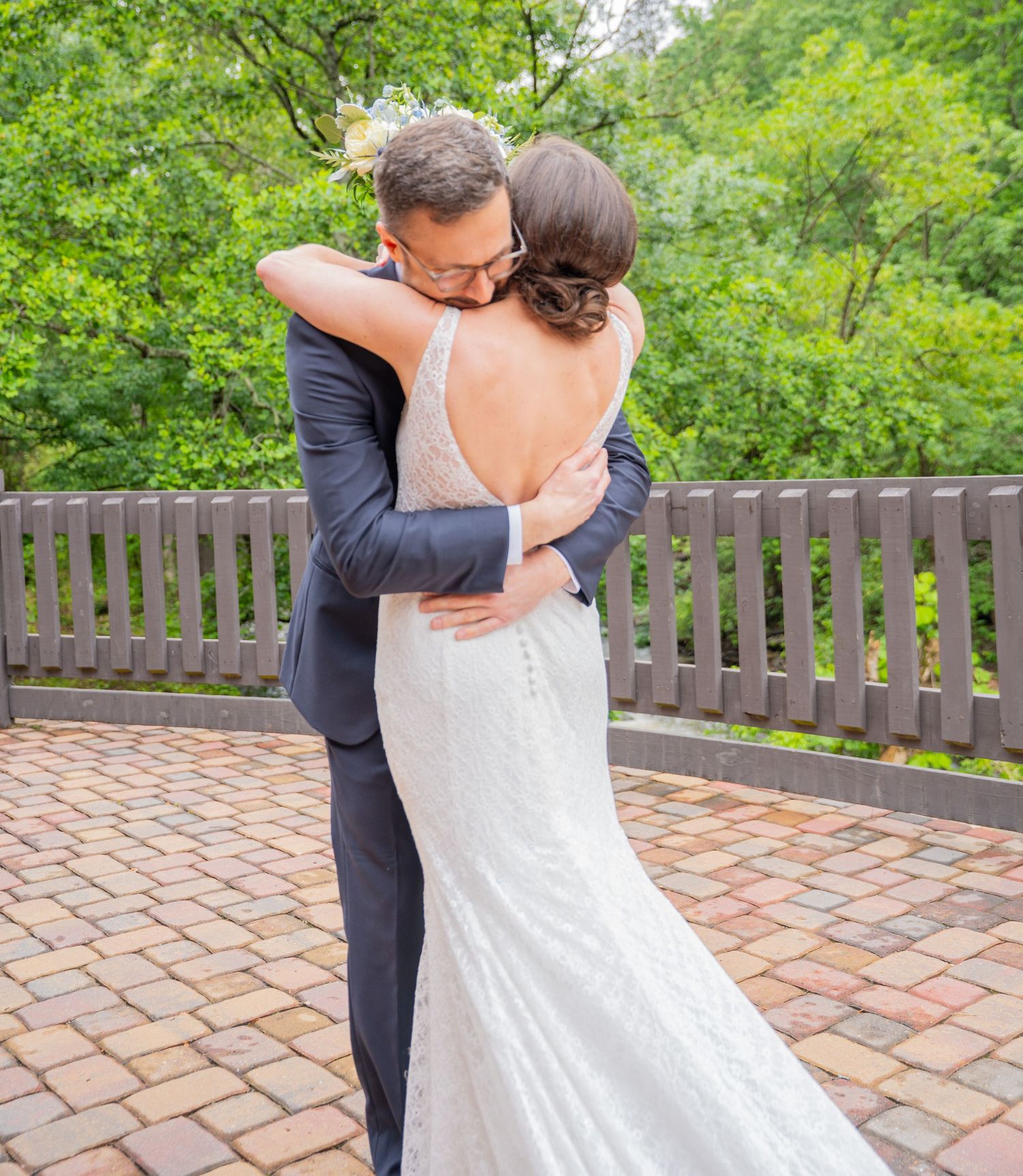 A couple embraces on a brick patio with lush green foliage in the background.