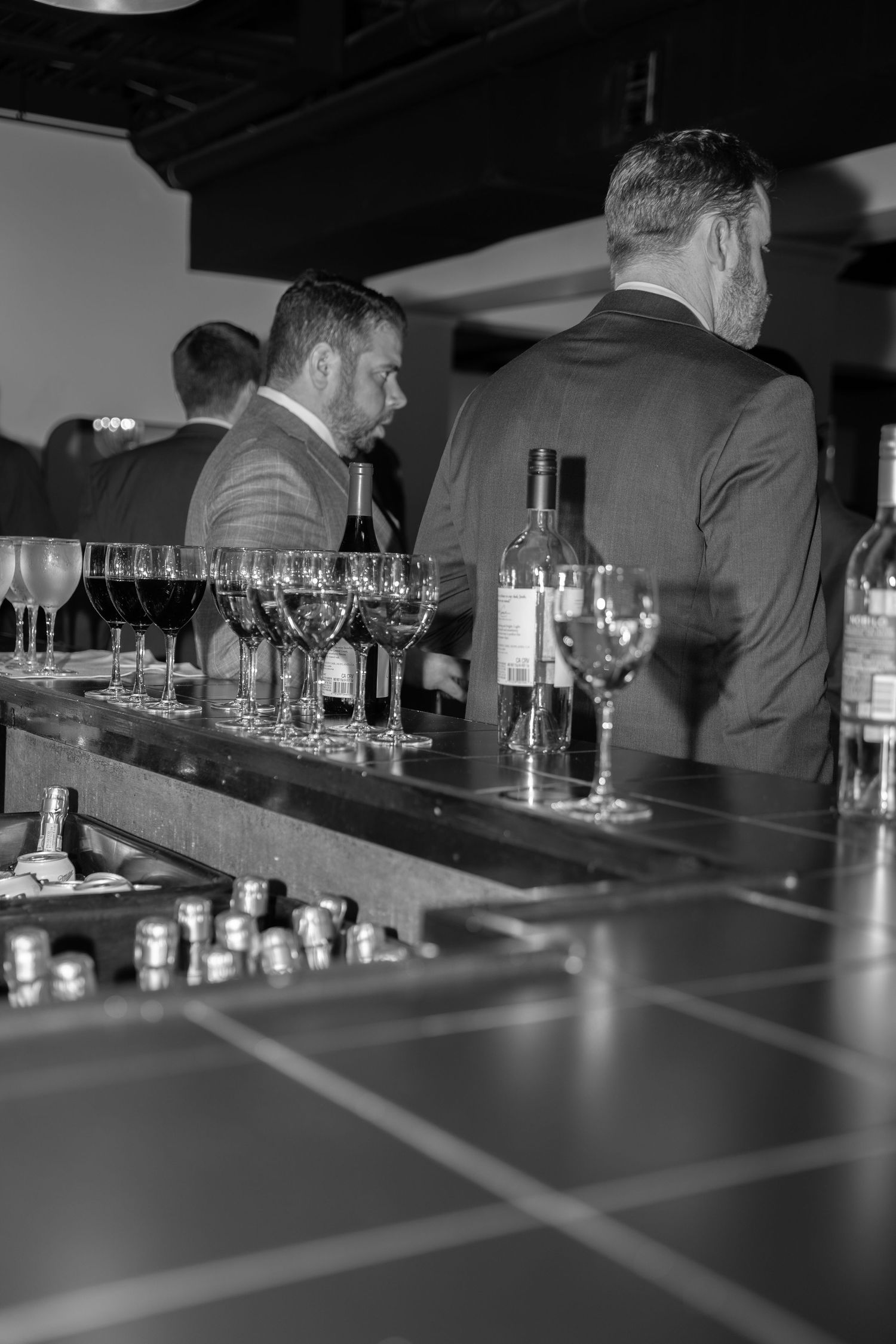 Black and white photo of bartenders behind counter with wine glasses and bottles at an upscale establishment.