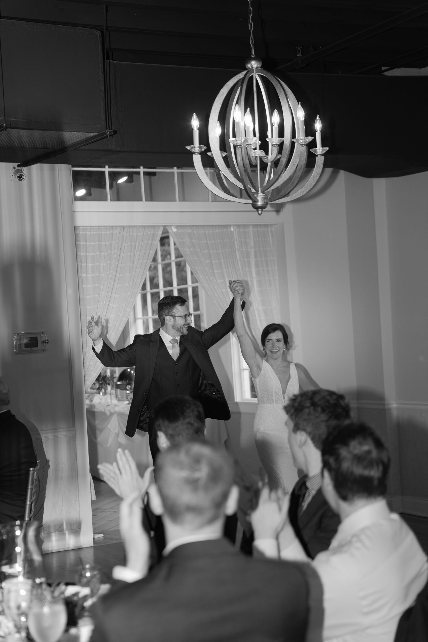 Black and white reception photo showing a celebratory entrance with an elegant chandelier overhead.