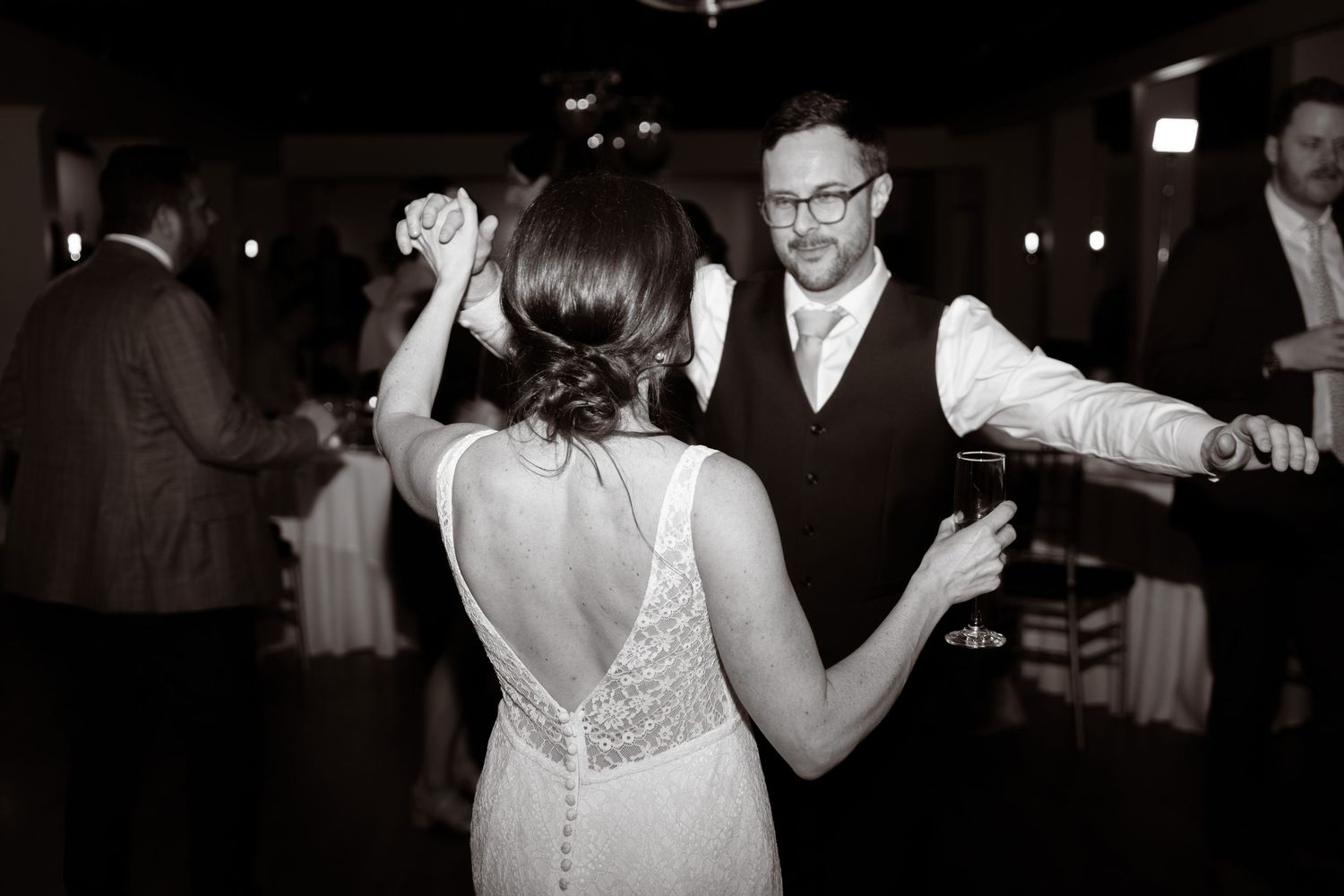 A couple dances together at a wedding reception, with the bride wearing a backless lace dress in black and white.