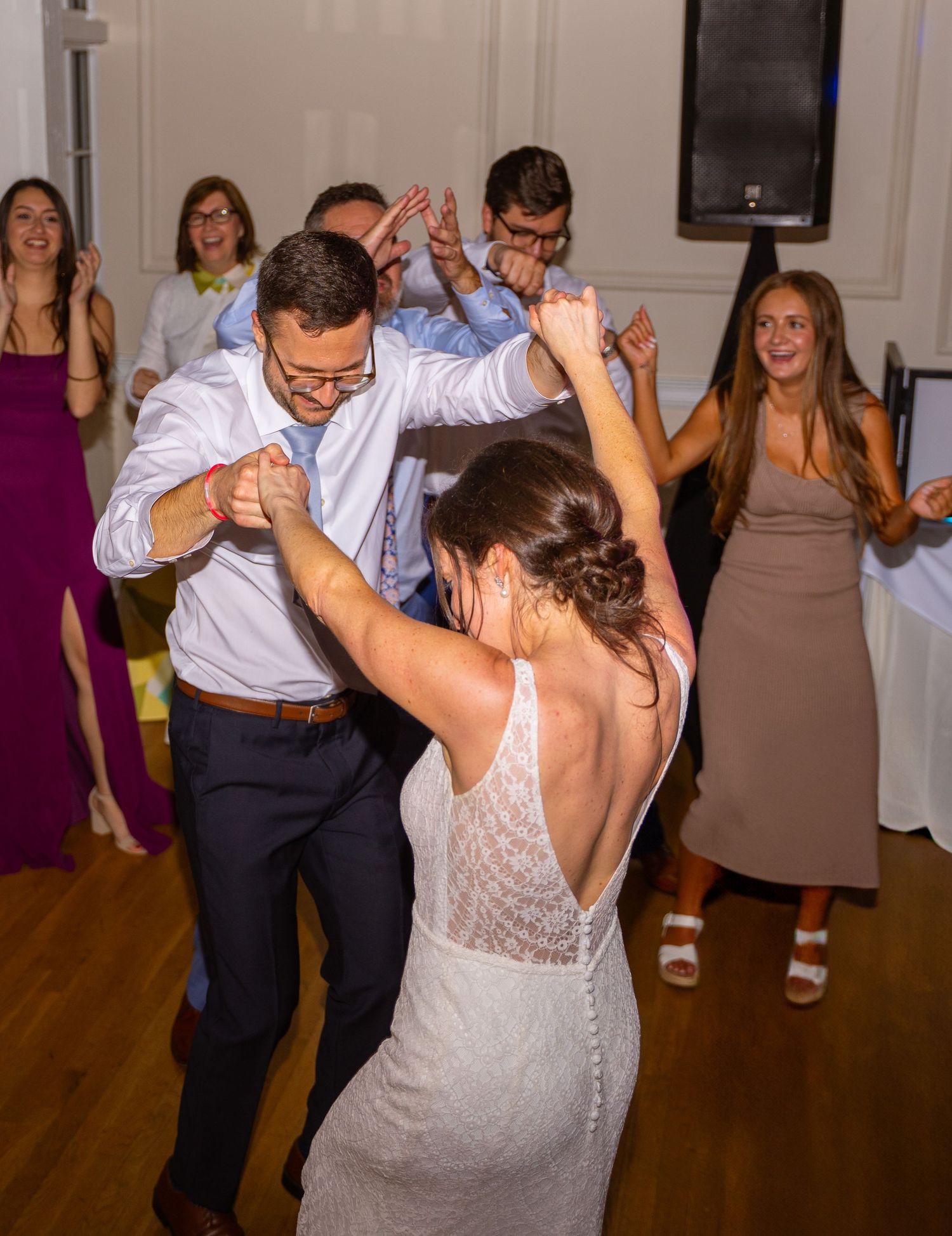 Wedding guests dance energetically on a hardwood floor during a lively reception celebration.