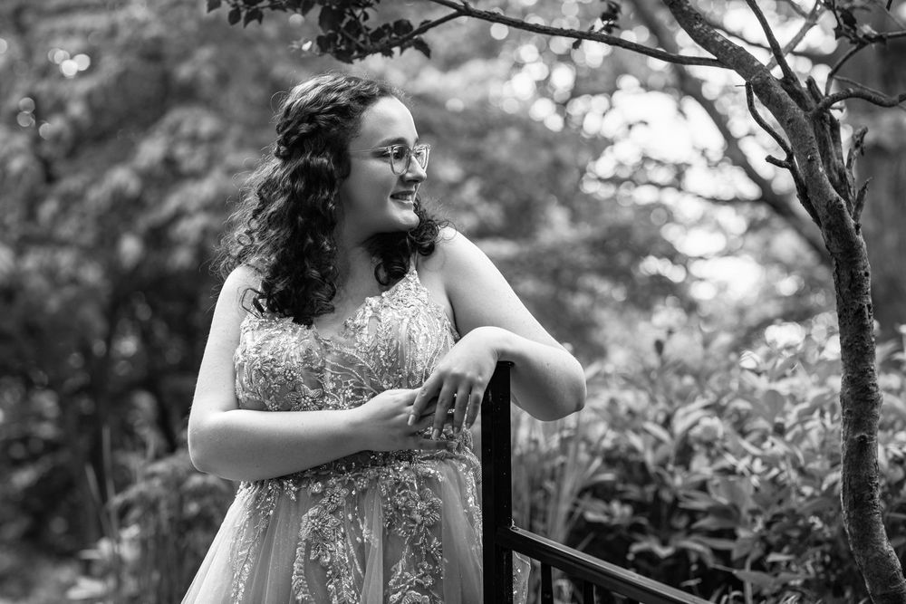 A joyful figure in a floral dress stands among trees in a natural outdoor setting during a photo session.
