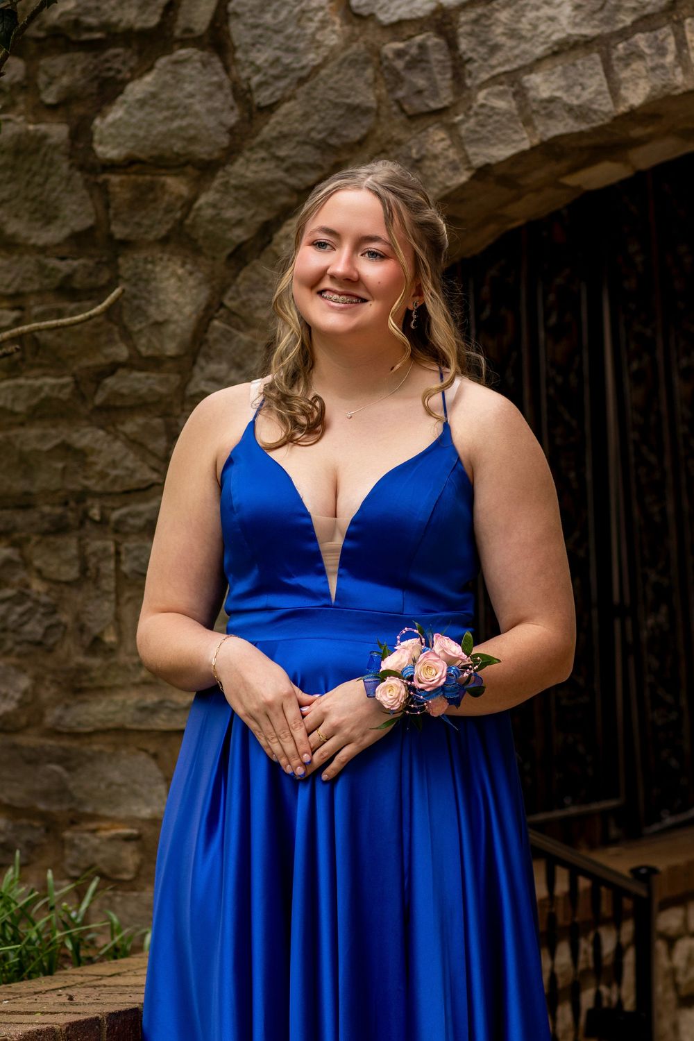 Person in a vibrant royal blue formal dress poses against a rustic stone wall backdrop.