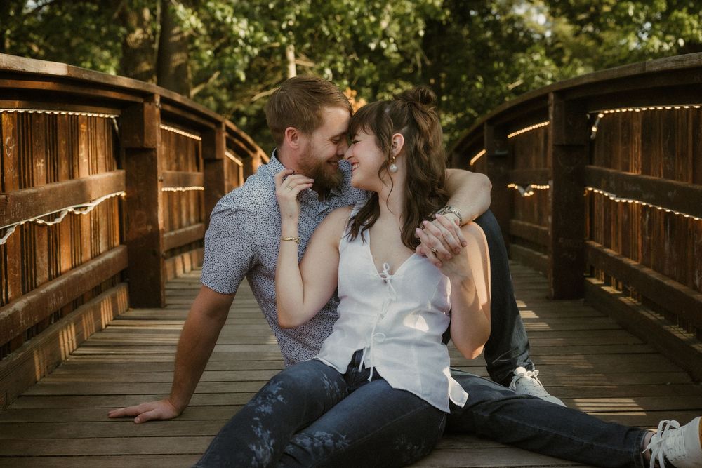 A romantic couple shares an intimate moment while sitting on a wooden bridge in warm evening sunlight at Loose Park in Kansas City.
