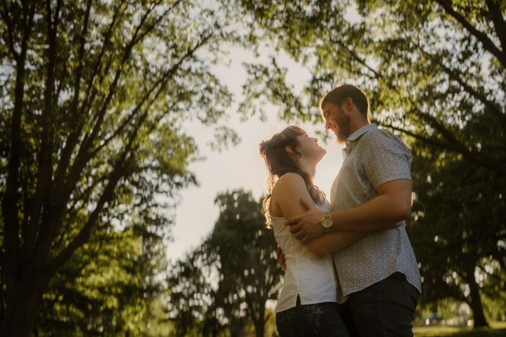 A couple embraces tenderly in golden sunlight beneath trees during a romantic outdoor photoshoot.