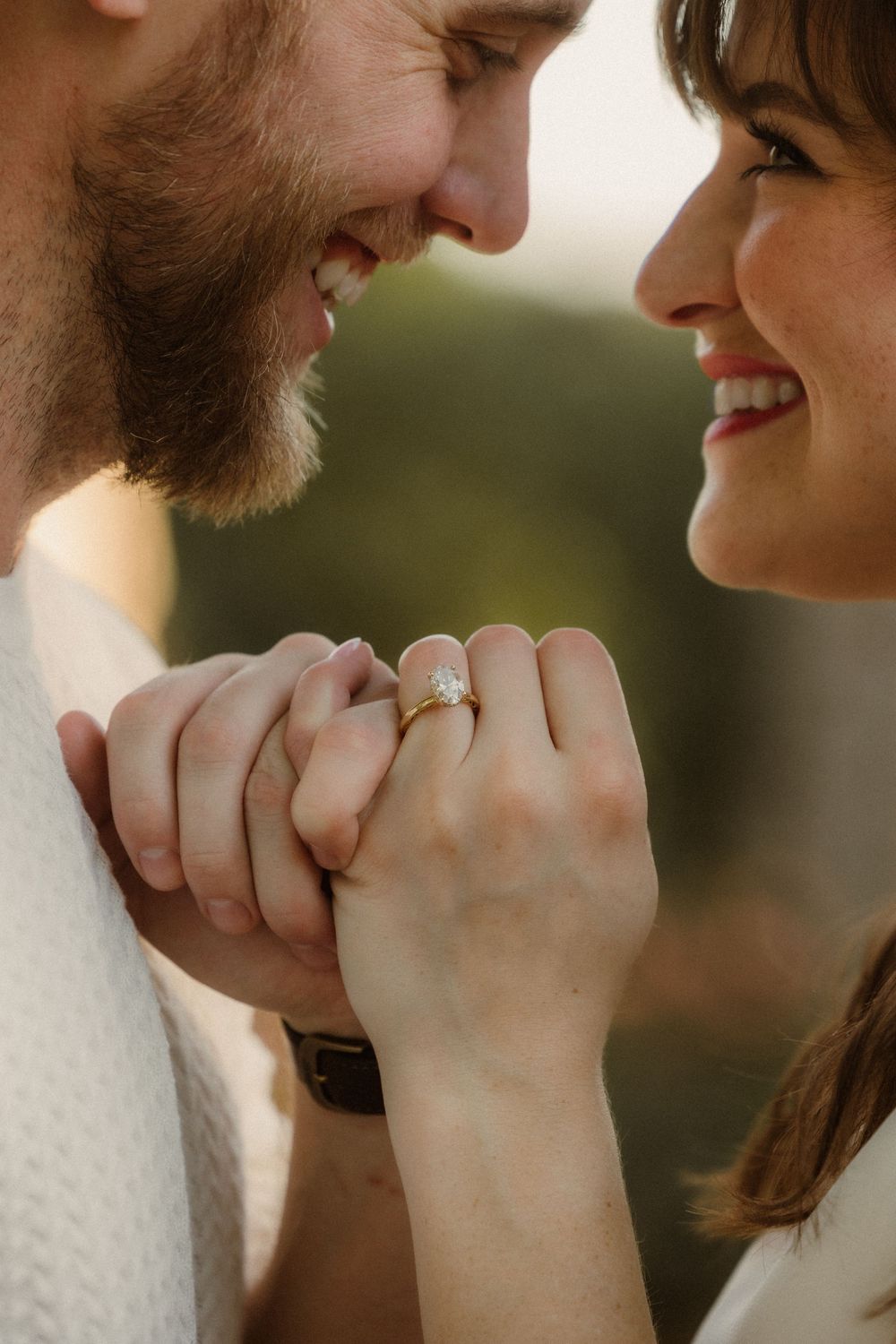 Close-up of couple's hands holding each other while showing off an engagement ring in soft natural lighting.
