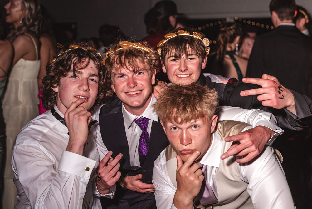 A group of young men in formal attire pose together at a celebration event with silly expressions.