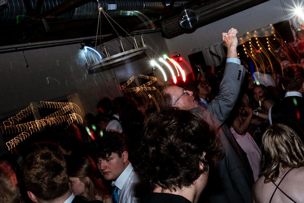 A crowded nightclub dance floor with people dancing under colorful disco lights and raised hands in celebration.