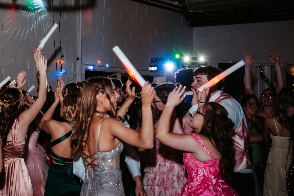 Energetic crowd dancing and celebrating with raised arms at a party with colorful lighting.