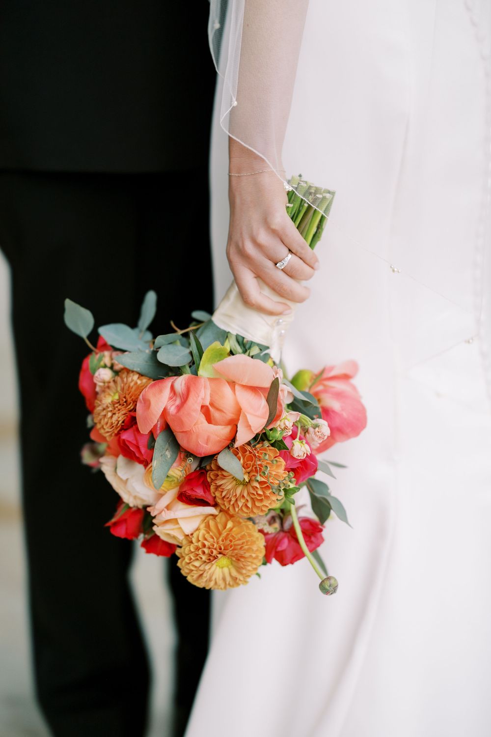 A bride in a white dress holds a vibrant coral and orange wedding bouquet with eucalyptus accents at Hall of Springs in Saratoga Springs, NY