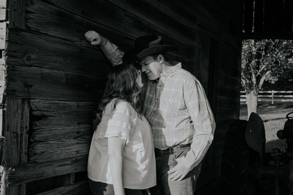 Black and white photo of couple standing by a rustic wooden barn wall having an intimate conversation.